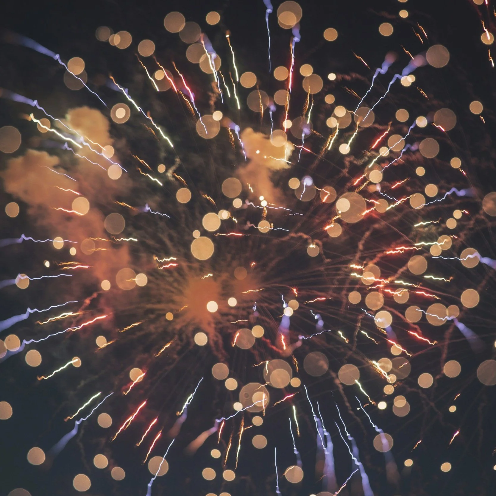 Feuerwerke explodieren am Nachthimmel, mit bunten Lichtstrahlen und Bokeh-Effekten.