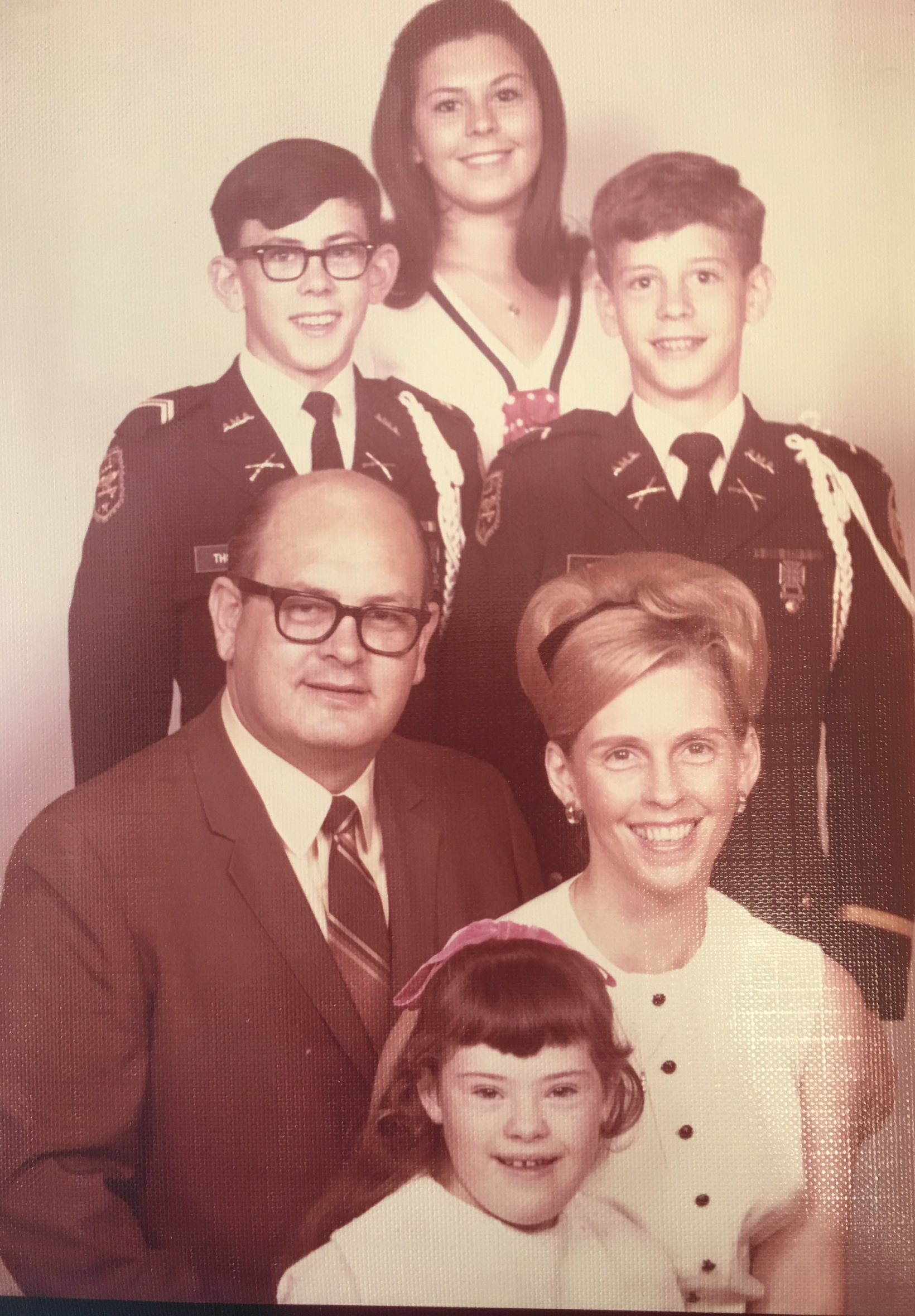 A family photo with six members, including children in scout uniforms, a woman, and a man in a suit, all smiling and standing against a plain background.