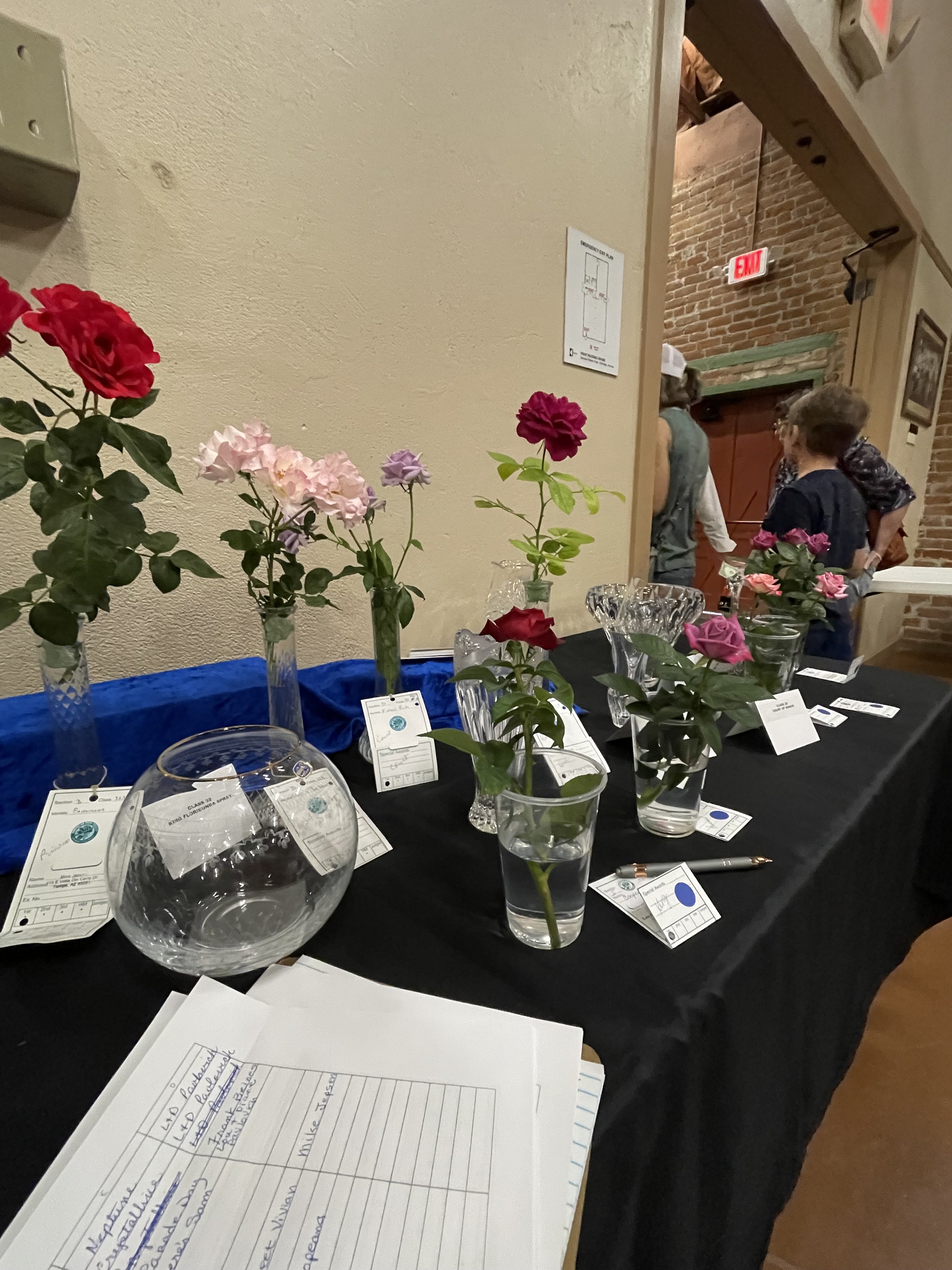 Table decorated with various colored roses in vases, some with price tags, and a blank notepad filled with handwritten notes placed on a black tablecloth.
