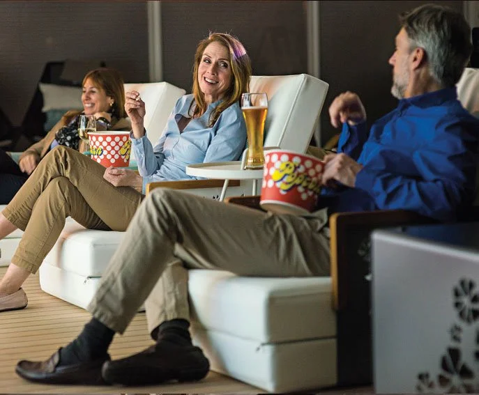 Three people sitting in reclining chairs, watching a movie, with popcorn and drinks, enjoying a movie night in a home theater. Emerald River Cruise.