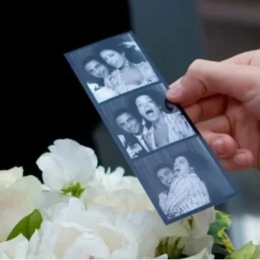 Person holding a black-and-white photo strip with four pictures of children, near white flowers.