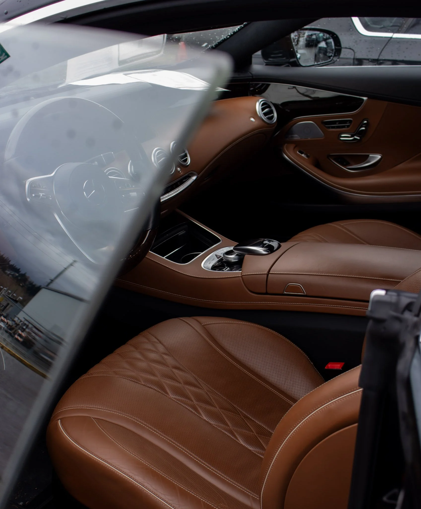 Interior of a luxury car with brown leather seats and a sleek dashboard, viewed from outside through the windshield and side window.