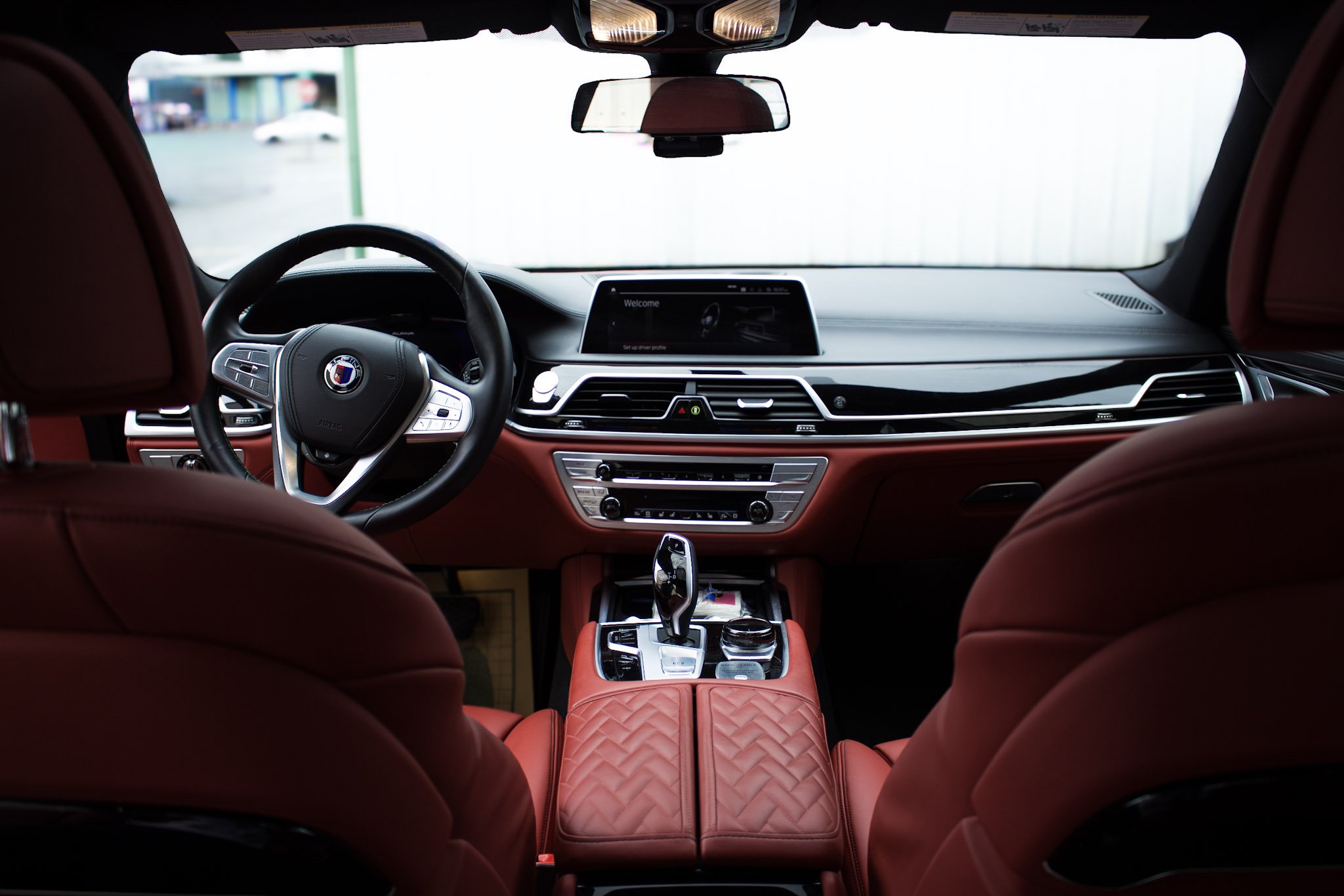 Interior view of a rare BMW Alpina B7 car with red seats, black dashboard, steering wheel with a BMW logo, and a central display screen, gear shift, and control knobs.