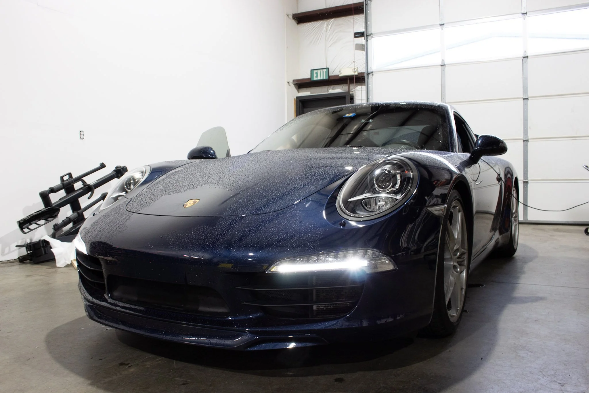 A dark blue Porsche sports car with water droplets on its surface, parked inside a garage.