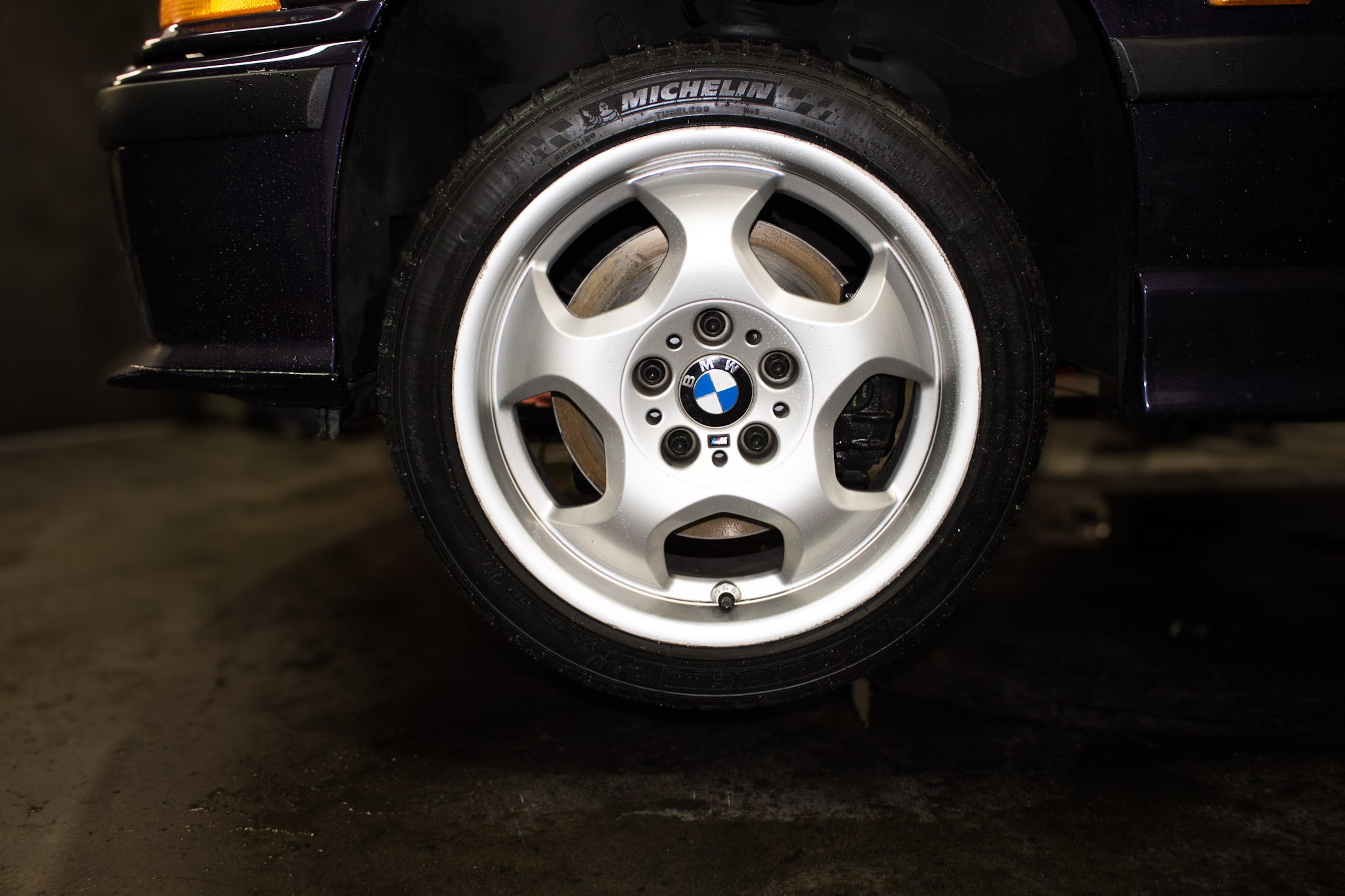 Close-up of a BMW car wheel with a silver rim and a black tire with Michelín branding, parked on a concrete surface.