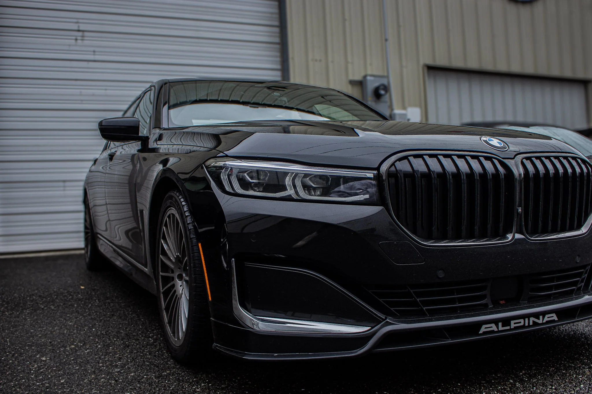 A rare black BMW Alpina B7 car parked outside near a beige building with a metal door.