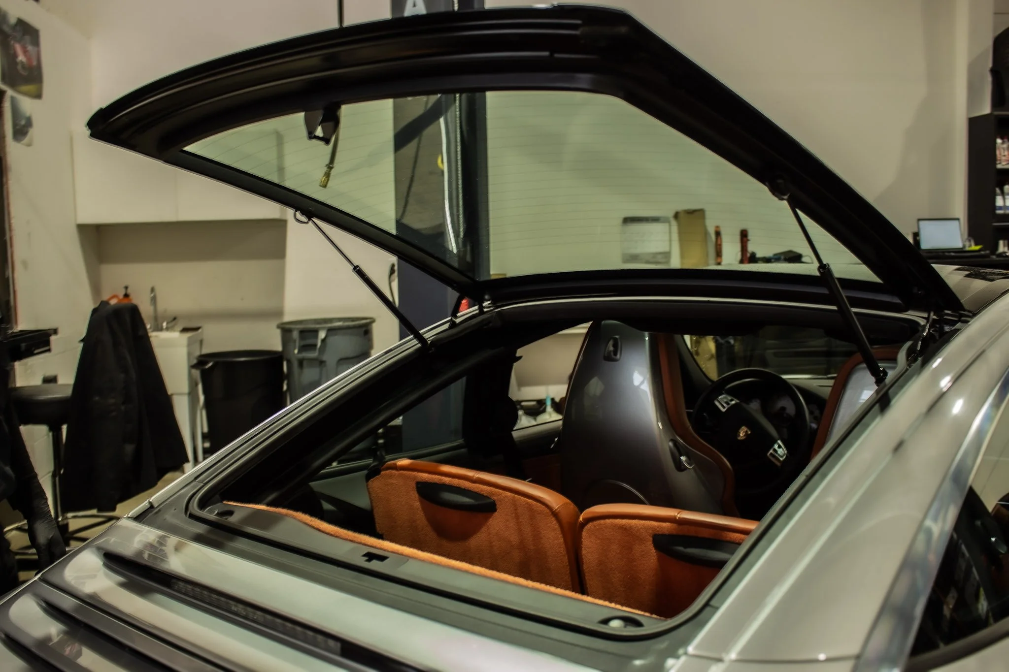 The interior of a Porsche targa with its trunk open, showing orange upholstery and black dashboard inside a garage.