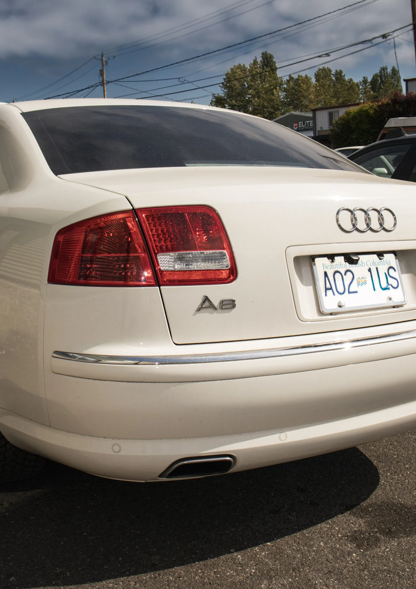 Rear view of a white Audi A6 car with a Washington state license plate, parked on a lot with some trees and buildings in the background.