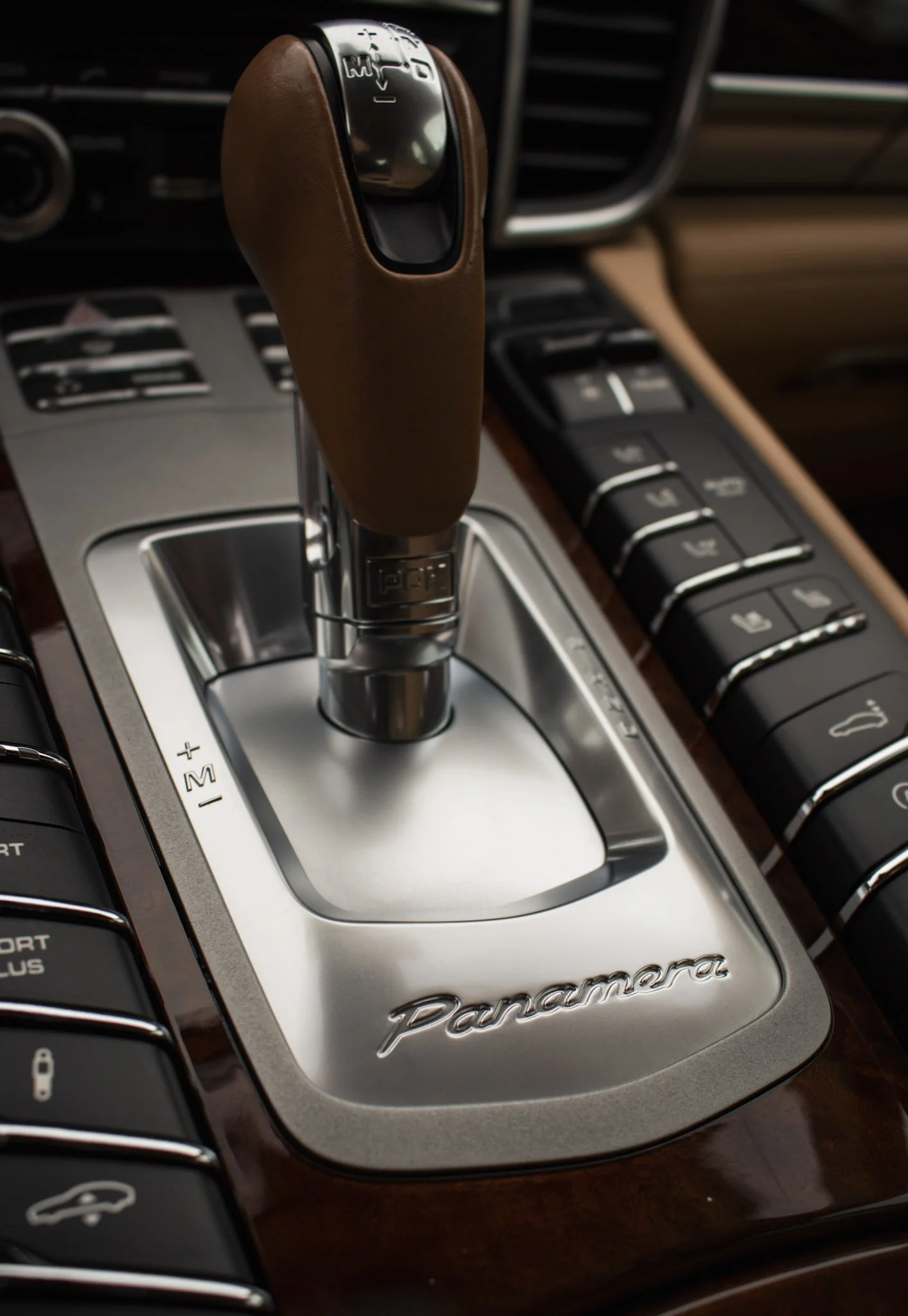 Close-up of a Porsche Panamera gear shift lever with a brown leather cover, surrounded by wood and metal trim in a luxury car interior.