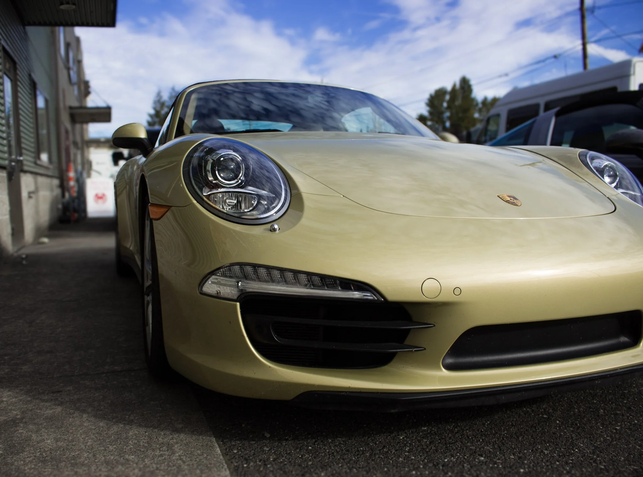 A rare gold Porsche sports car parked on a city street with a blue sky overhead.