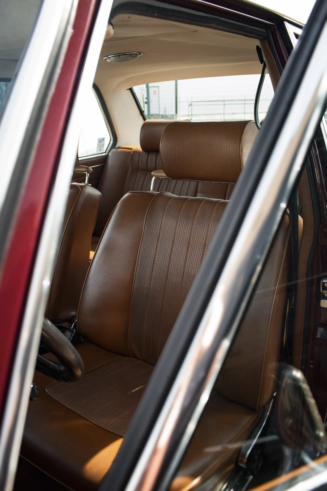 Inside of a vintage car with brown leather seats and a beige ceiling, viewed through the open window.