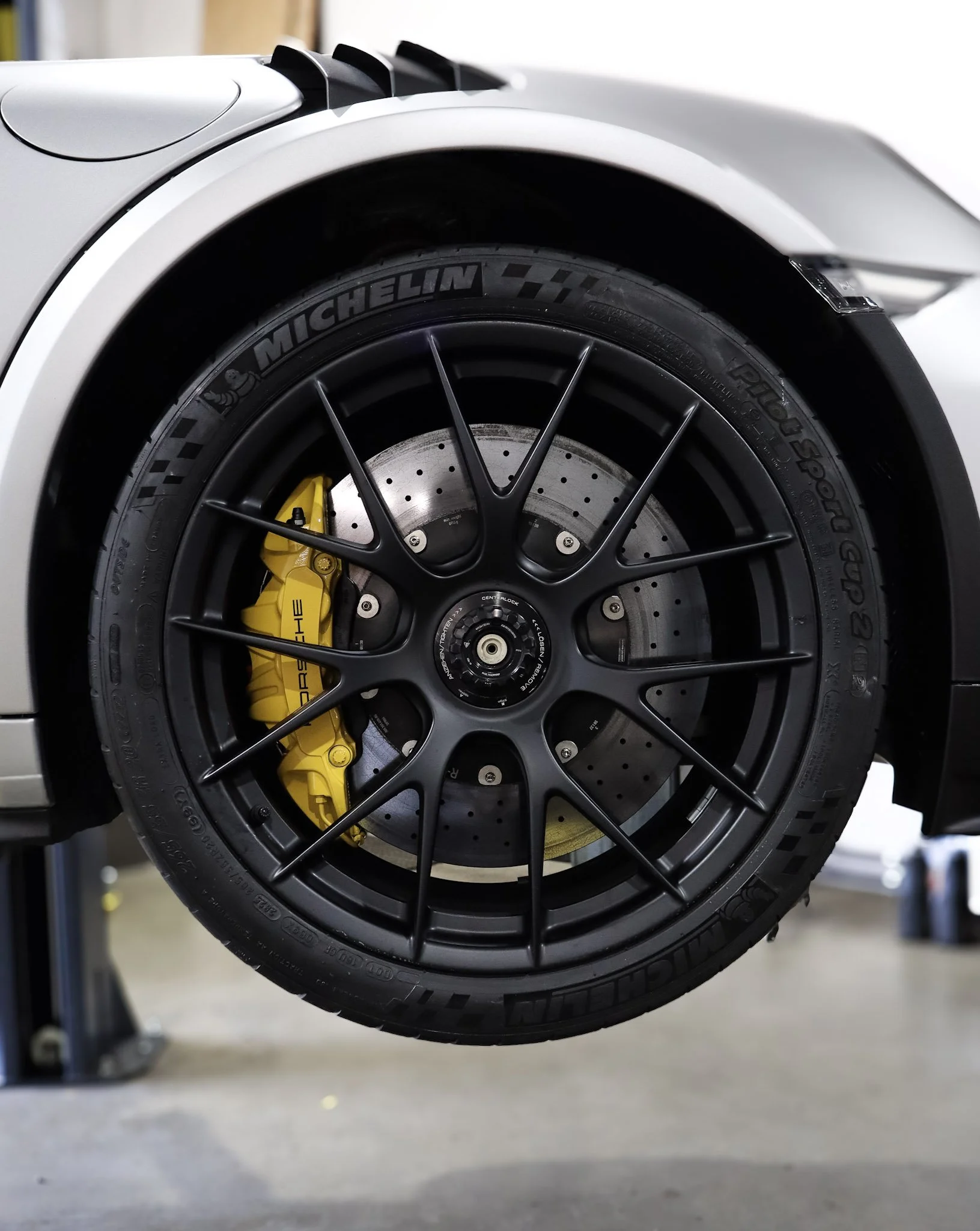 Close-up of a car's black wheel with a Michelin tire and a yellow brake caliper, with a white car body and a blurred background.