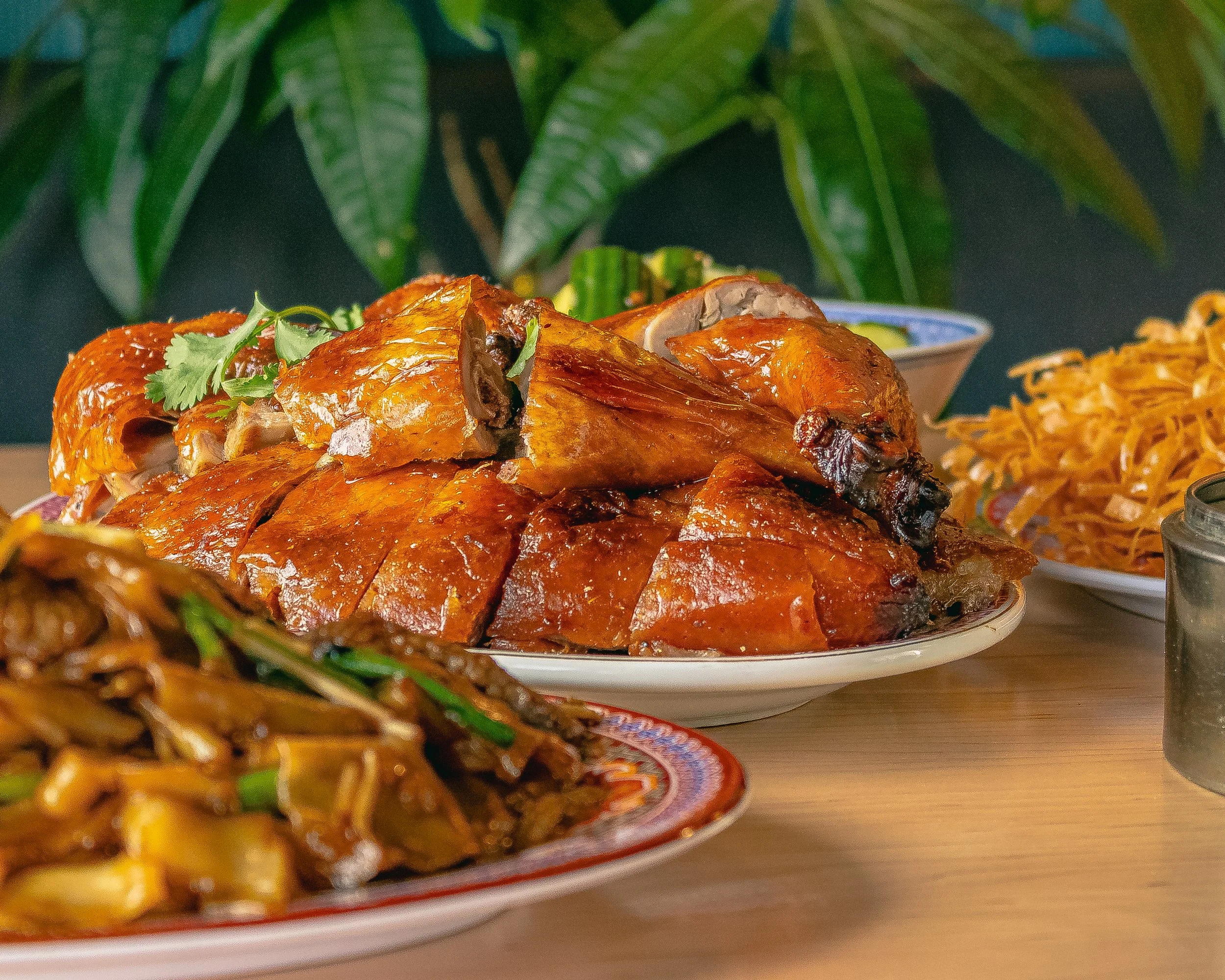 Roast chicken with vegetables and noodles on dishes, with a leafy green background.