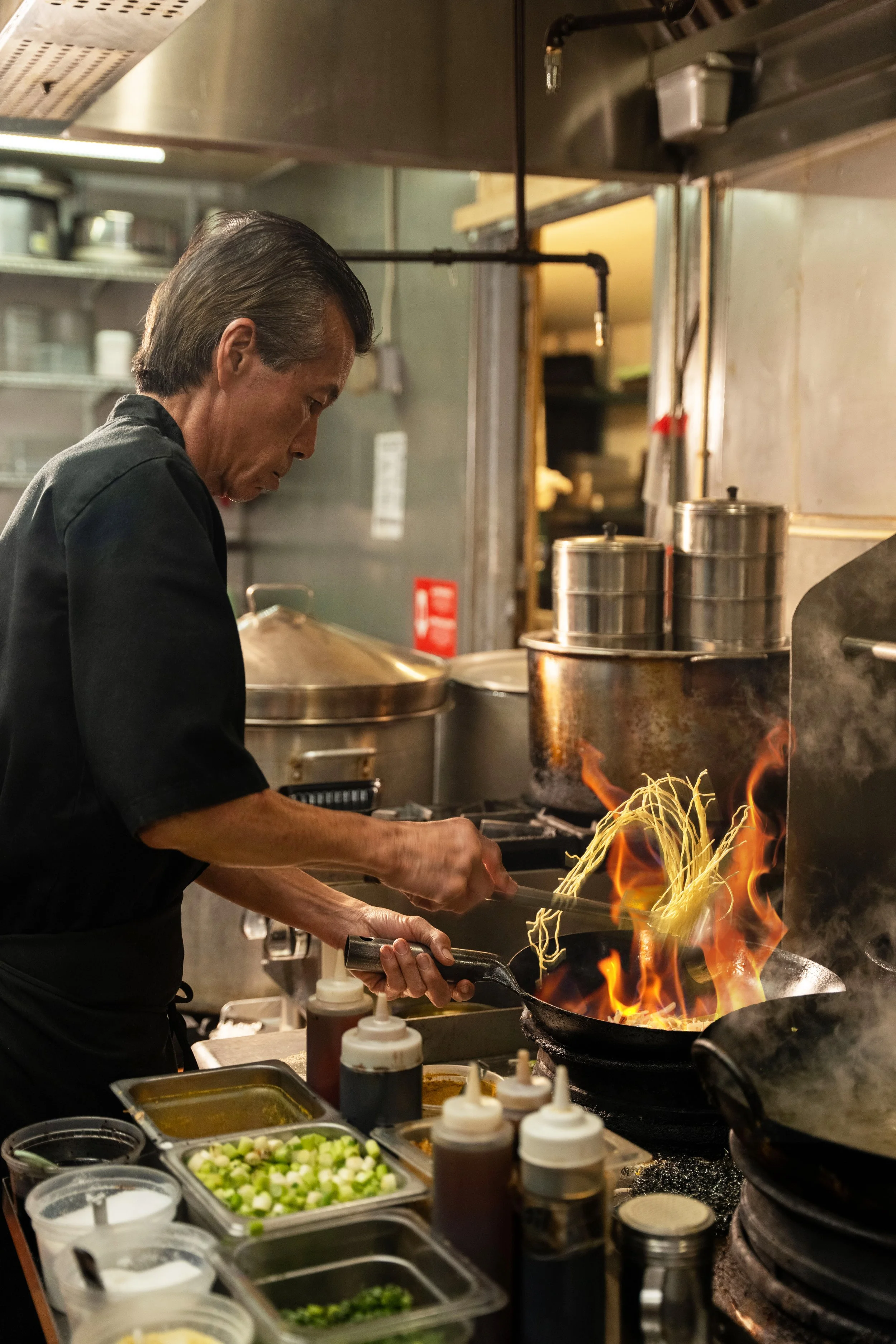 A chef cooking in a restaurant kitchen with ingredients and condiments on the counter.