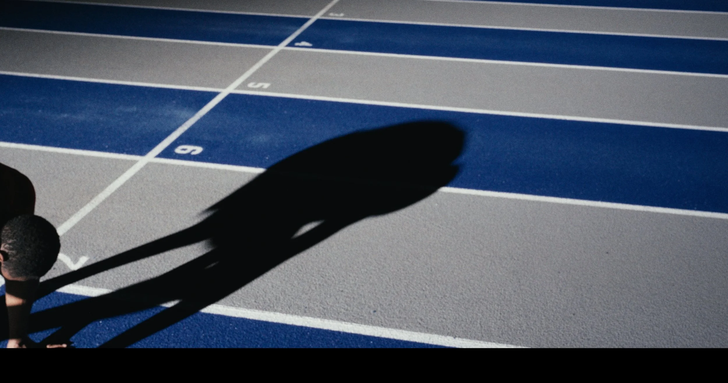 Shadow of a person on a running track with blue lanes and white lane markings.