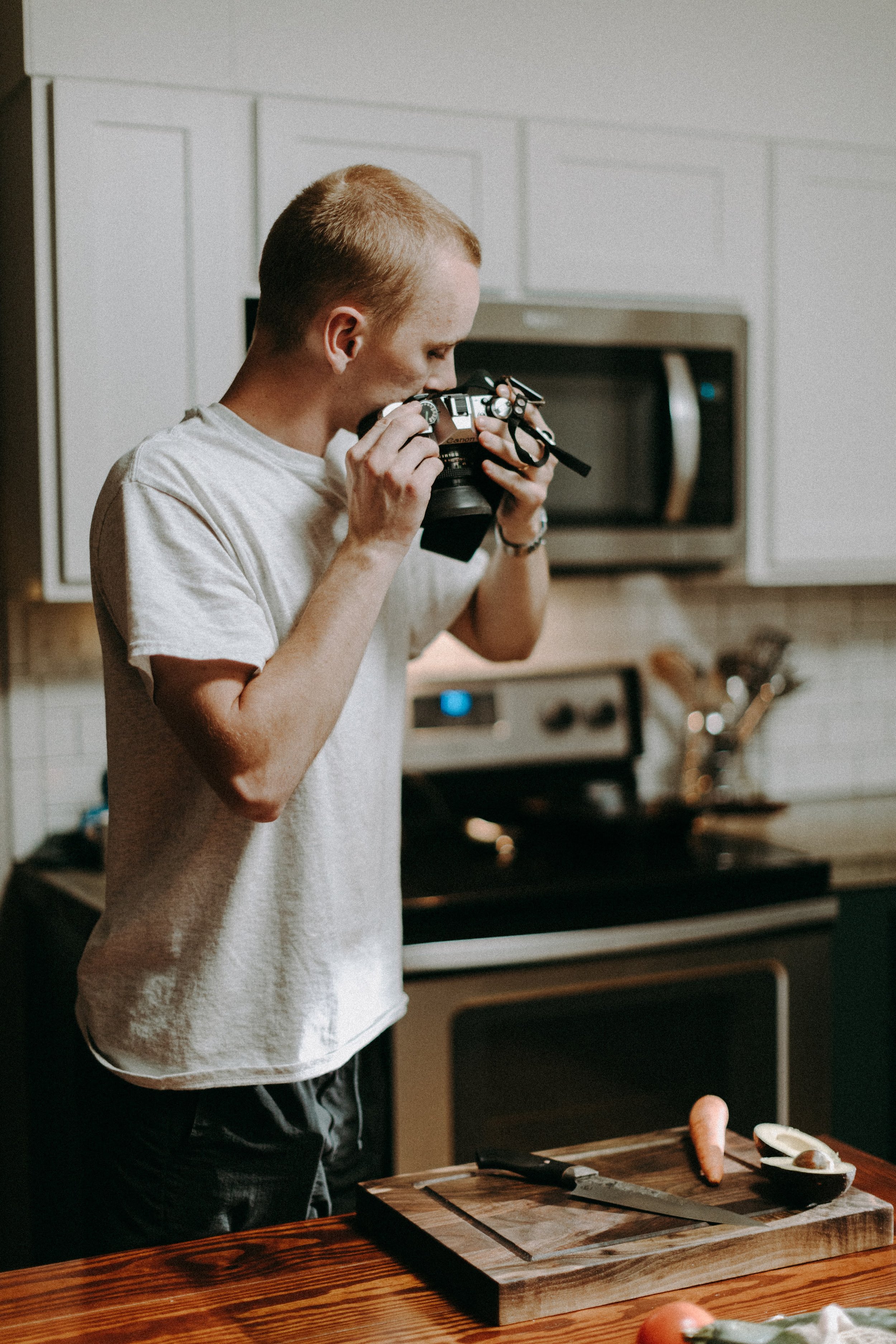 Person in kitchen taking photo of cutting board with carrots and avocados
