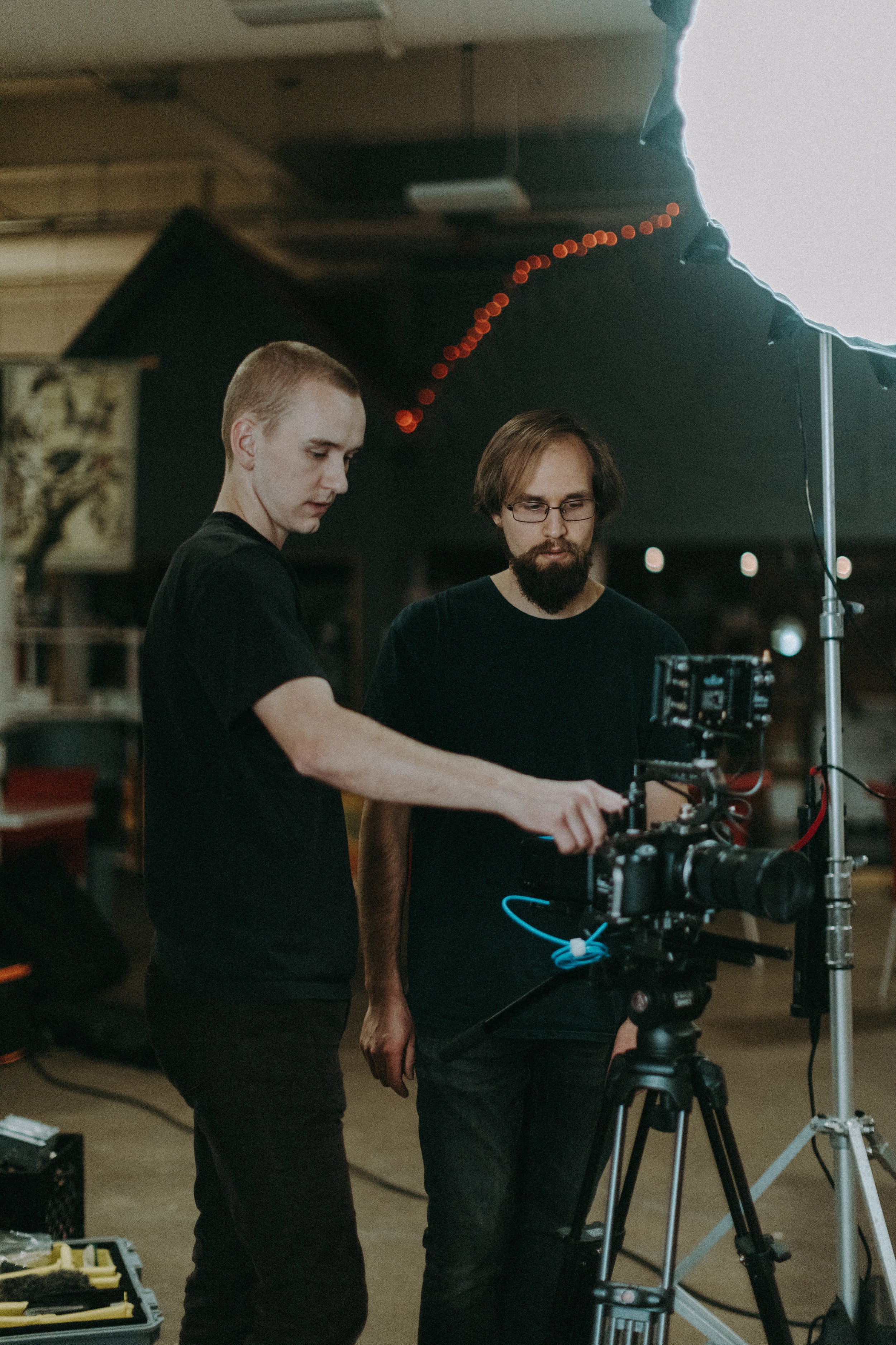 Two men in a studio adjusting camera equipment and lighting.