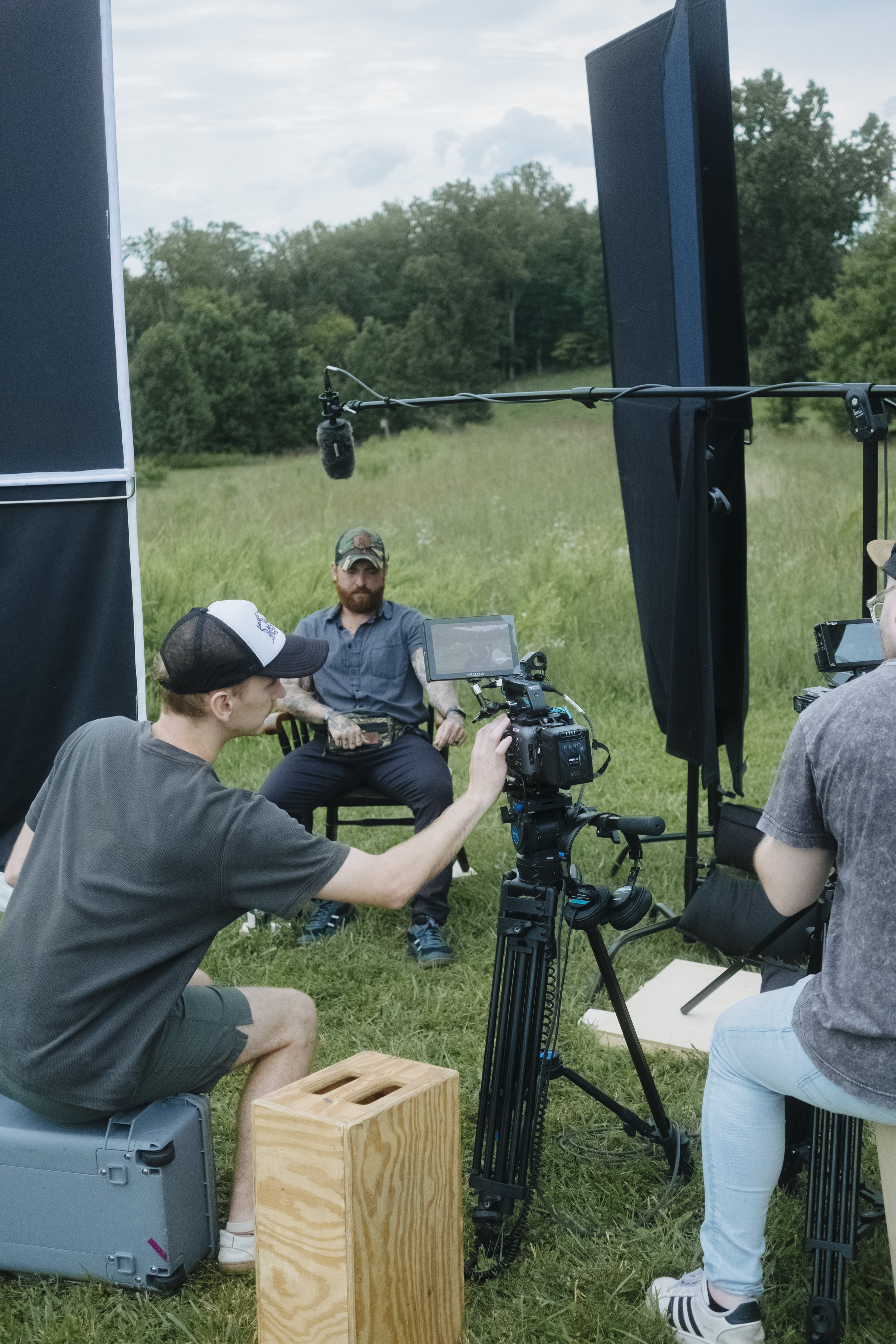 Outdoor film set with a man being filmed, surrounded by crew and equipment.