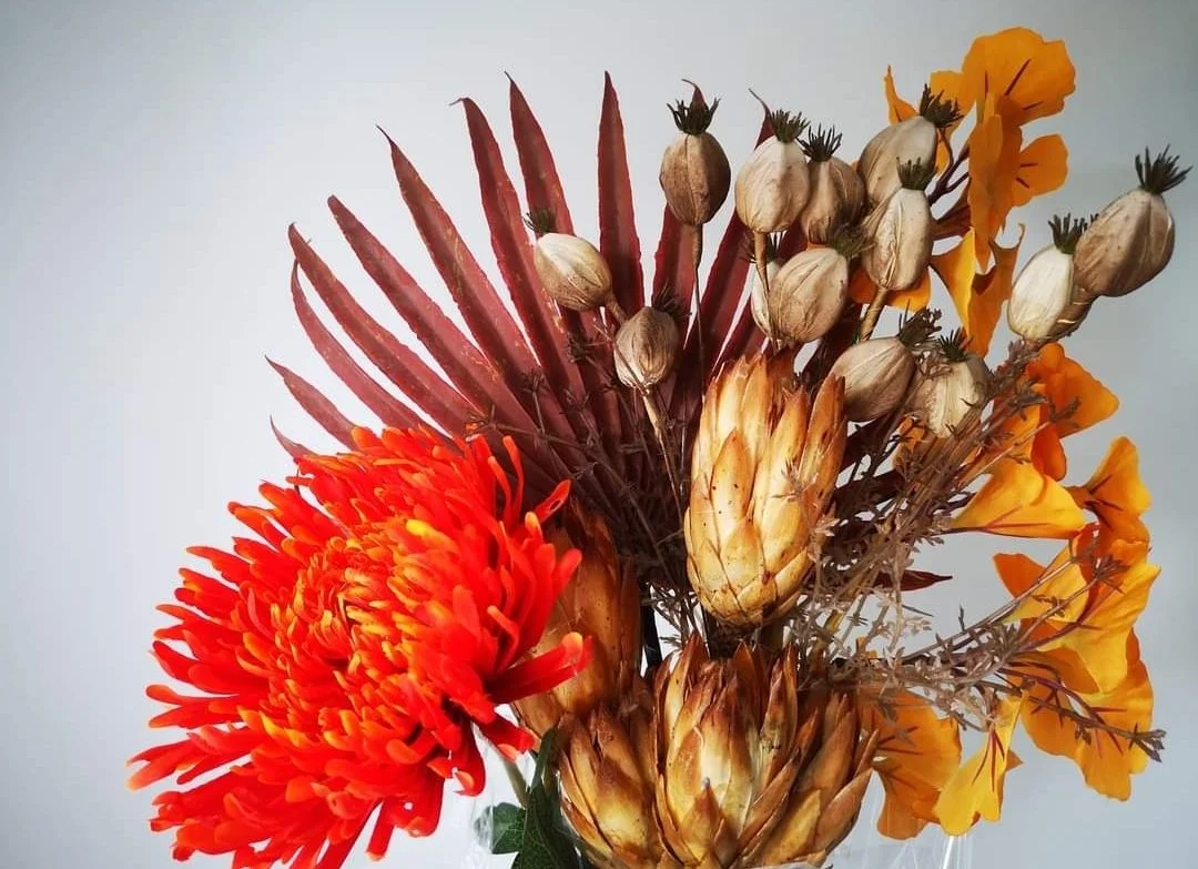 A bouquet of dried and fresh flowers, including a large orange chrysanthemum, yellow poppies, and other dried seed pods and flowers.
