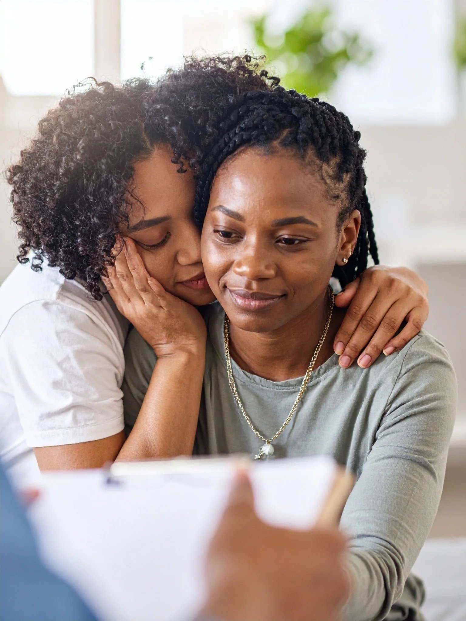 Two women sharing a tender moment, one whispering into the other's ear with a warm embrace.