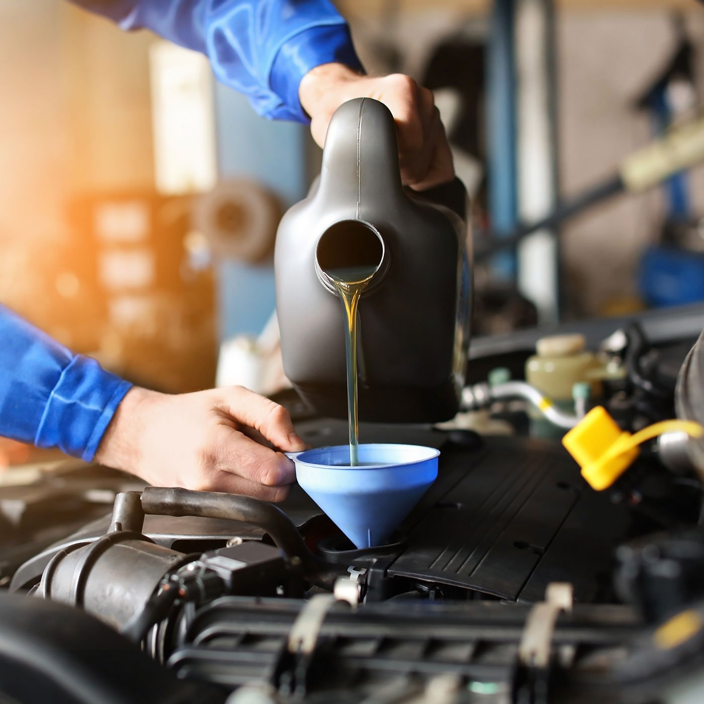 Person pouring motor oil into a car engine using a funnel