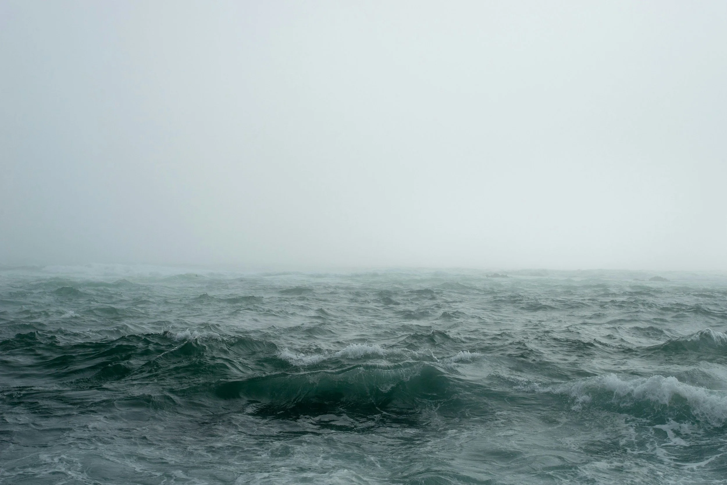 Rough ocean waves with misty, overcast sky in the distance.