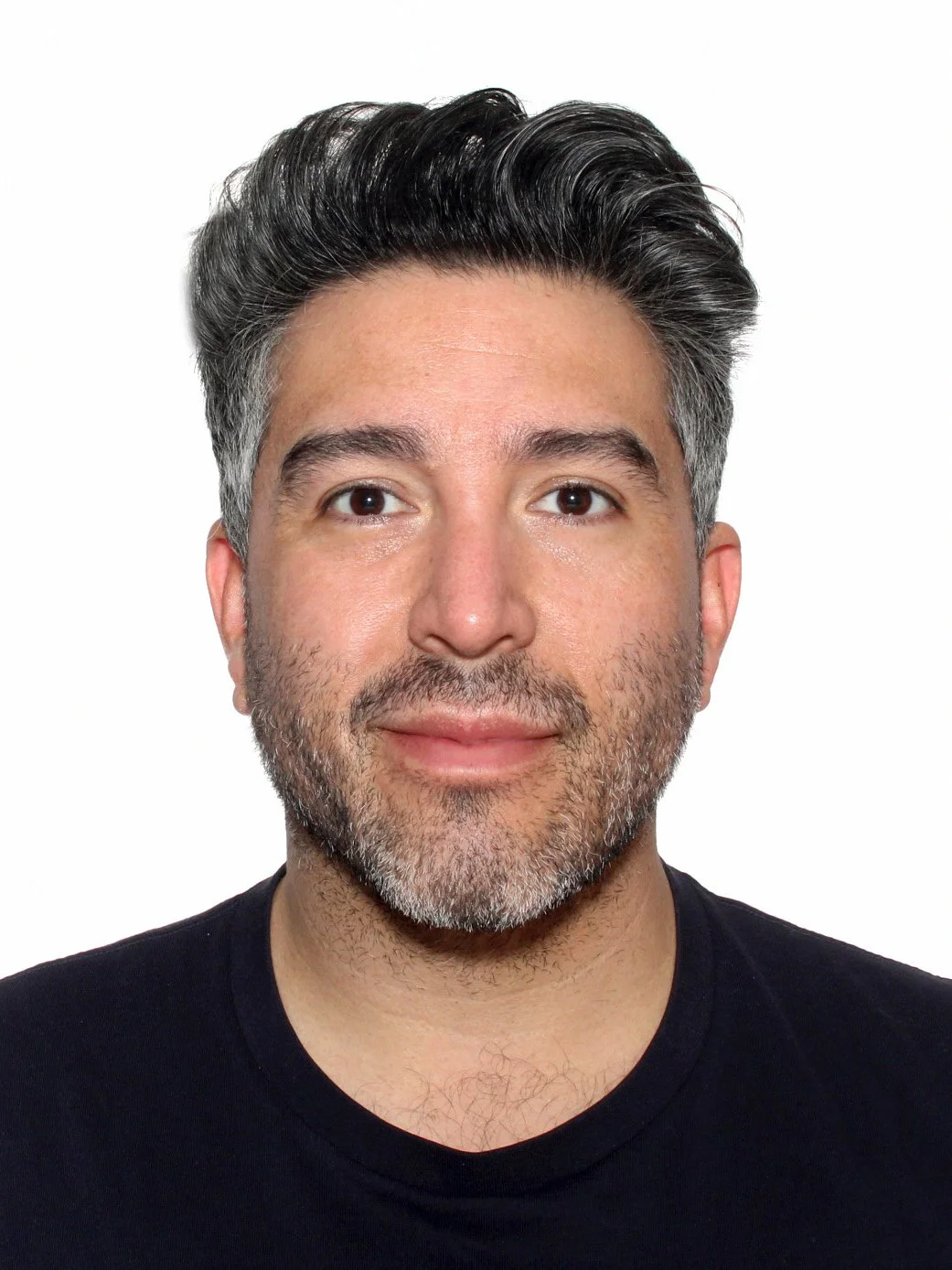 A close-up portrait of a man with dark and gray hair, facial hair, and a black shirt, set against a white background.