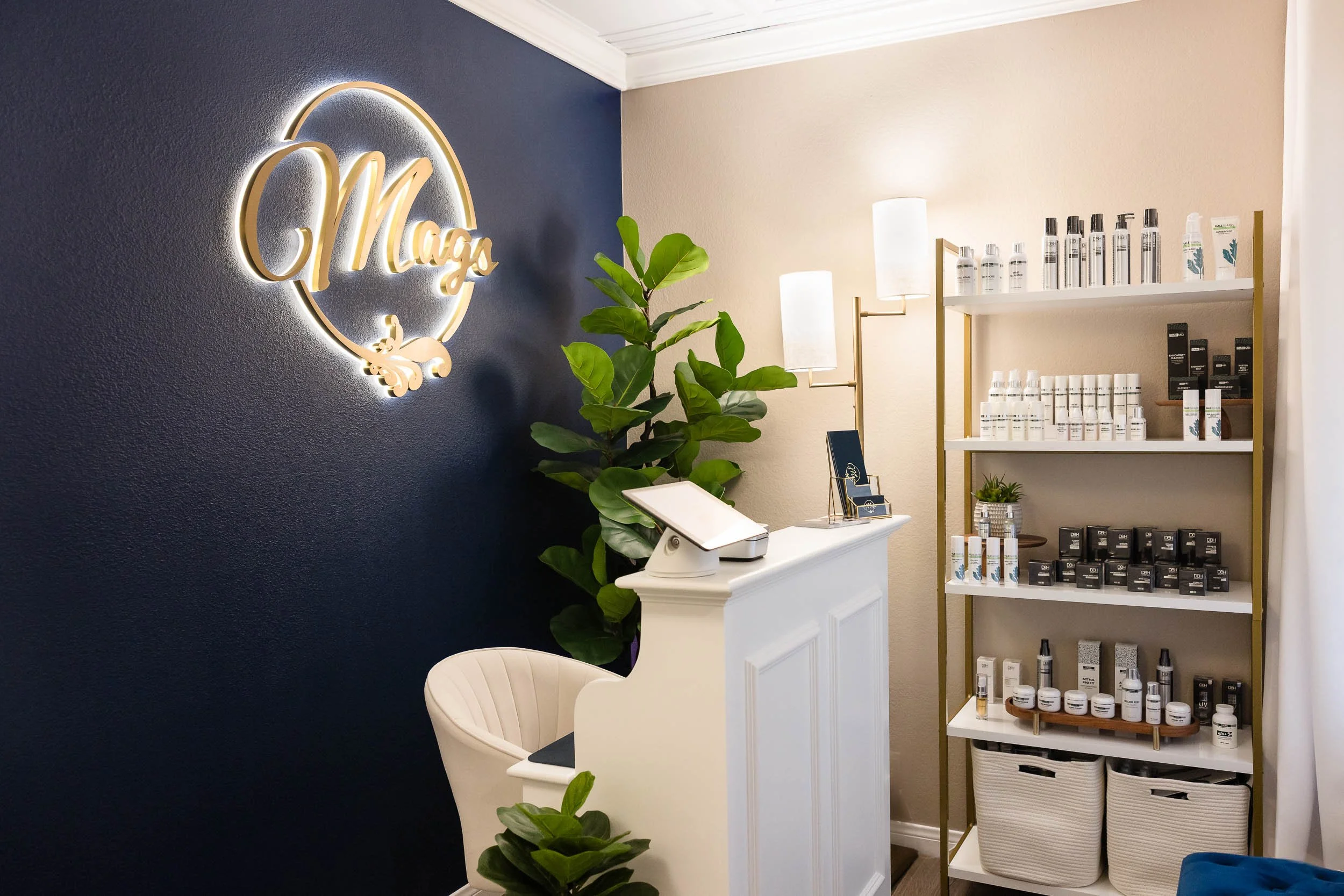 Photo of Mags Cathey Spa Lobby. Blue wall with gold Mags logos and White reception desk.