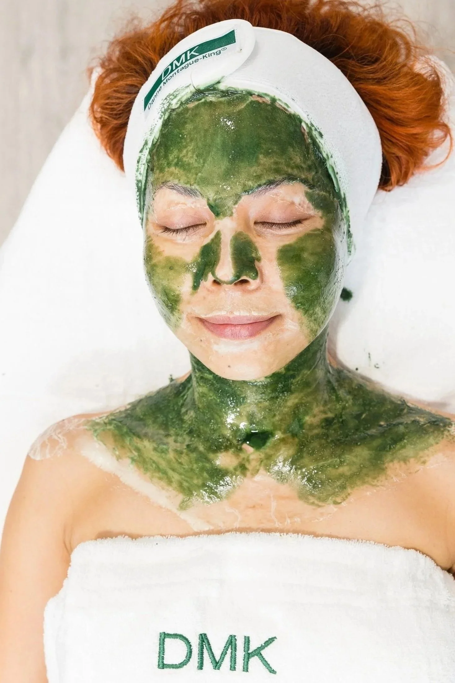 DMK facial green face mask applied on a caucasian woman with red hair.