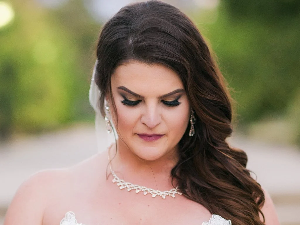 Bride looking down with elegant hairstyle and jewelry, blurred natural background.