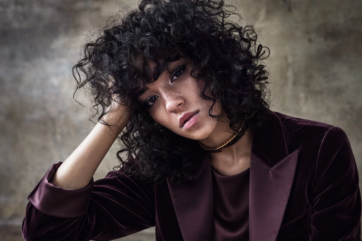 Curly-haired portrait in a burgundy jacket against a textured backdrop
