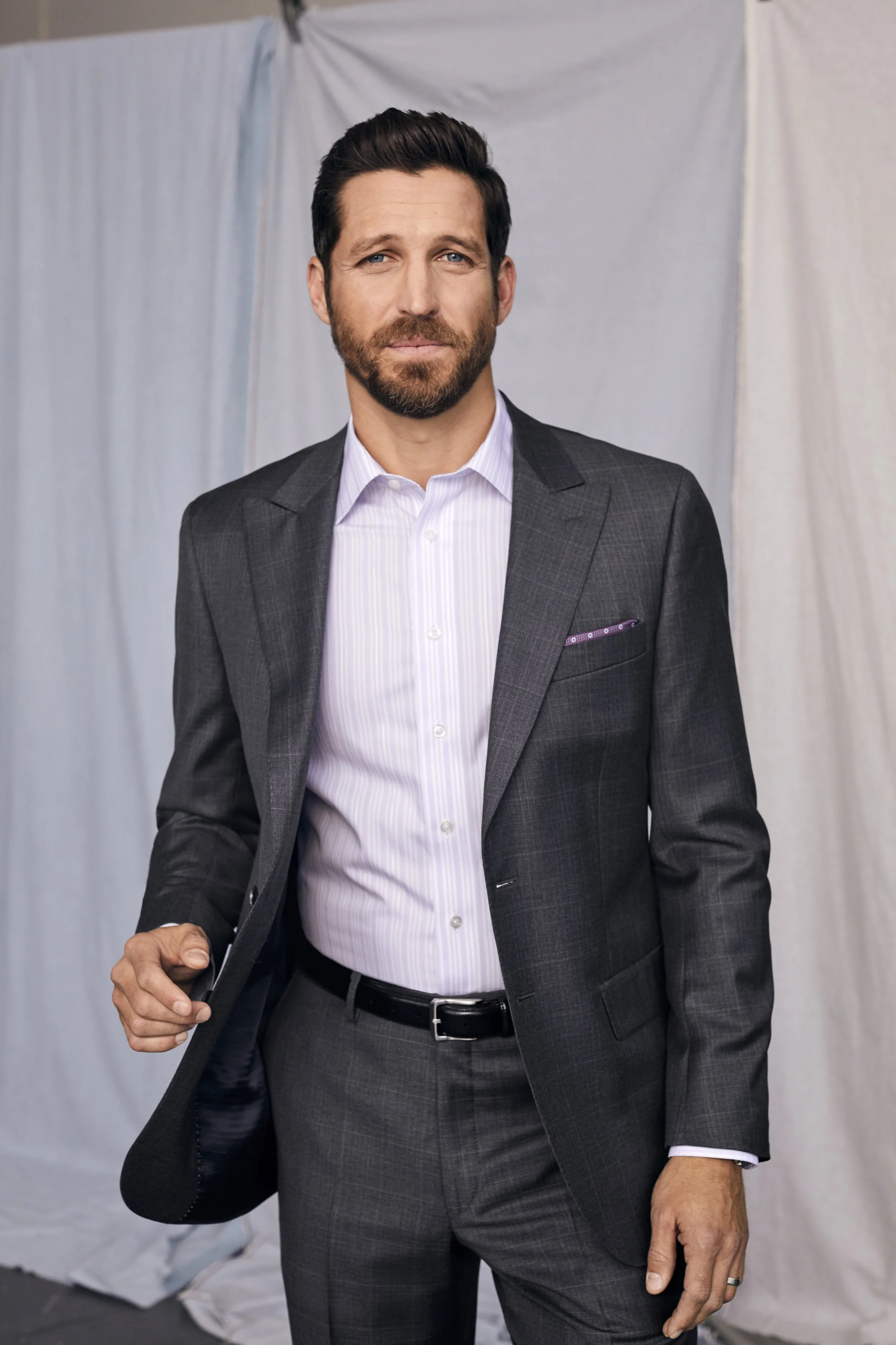 Portrait of a man in a gray suit against a draped backdrop