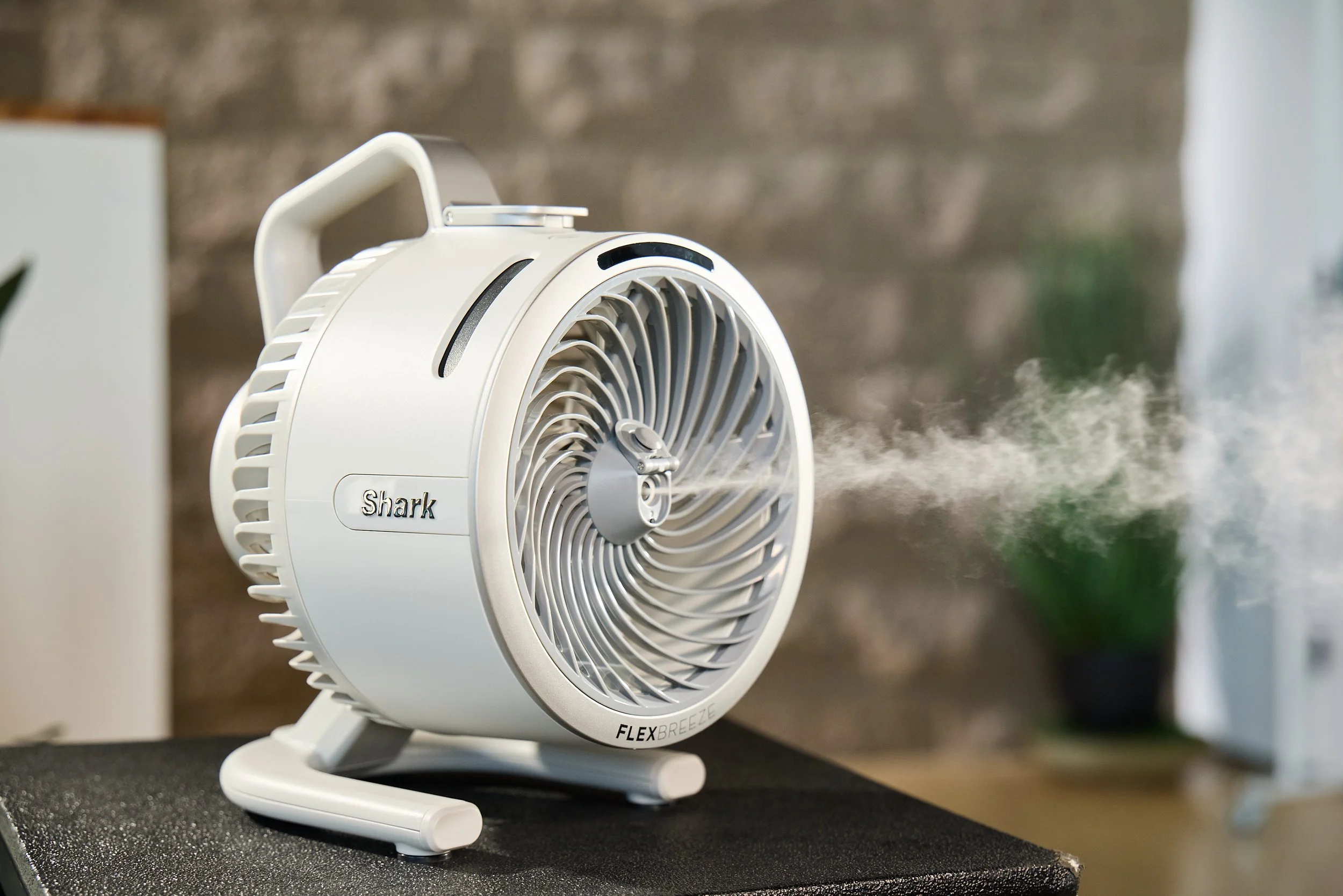 A white Shark Flex Breeze fan on a table, blowing mist indoors.