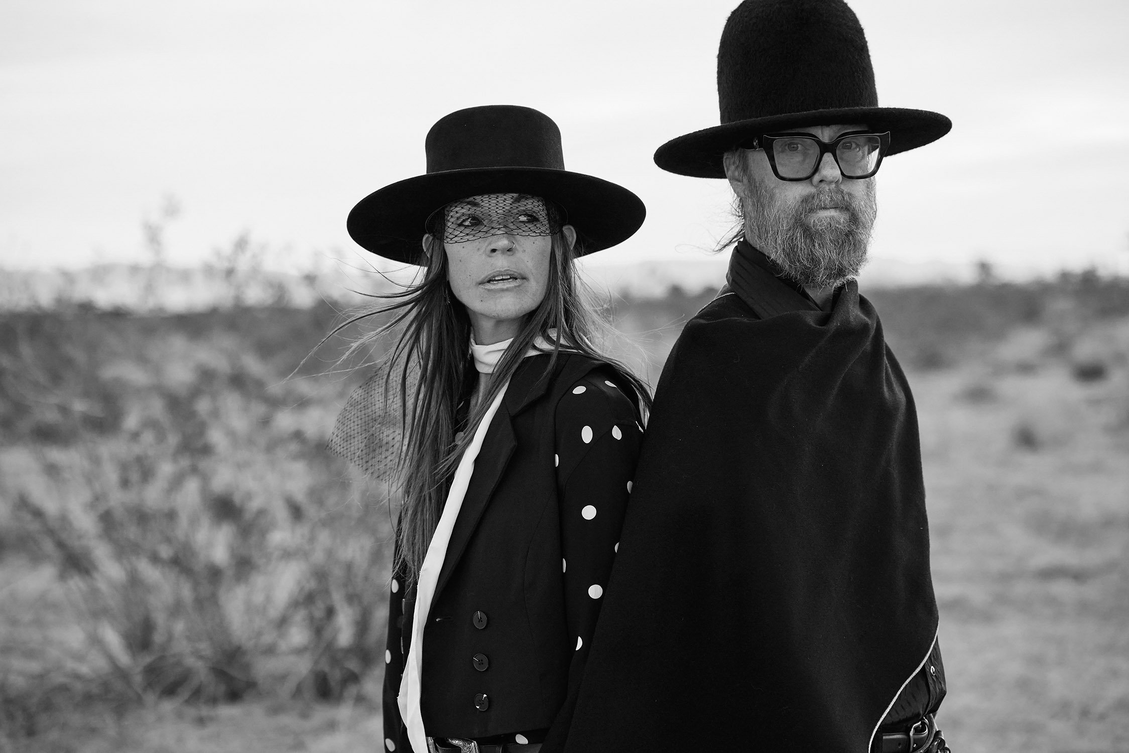 Black-and-white portrait of two people in wide-brimmed hats in an open landscape