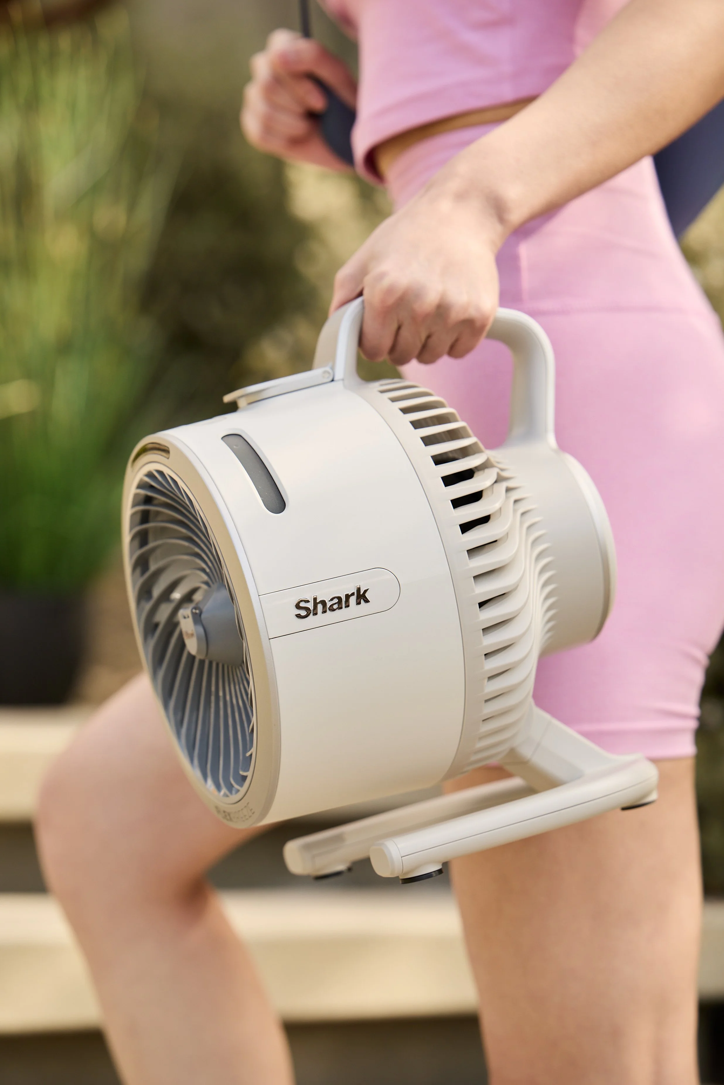 Person holding a portable Shark brand air purifier or fan, wearing pink exercise clothing.