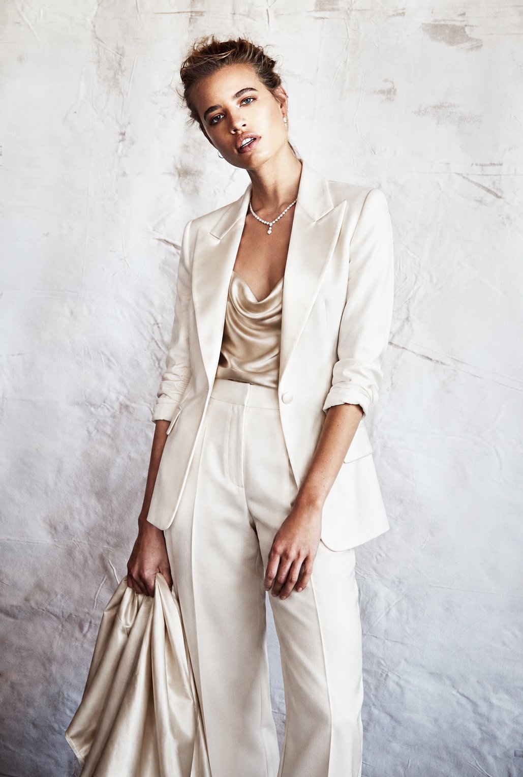 Standing portrait in a white suit against a pale textured backdrop