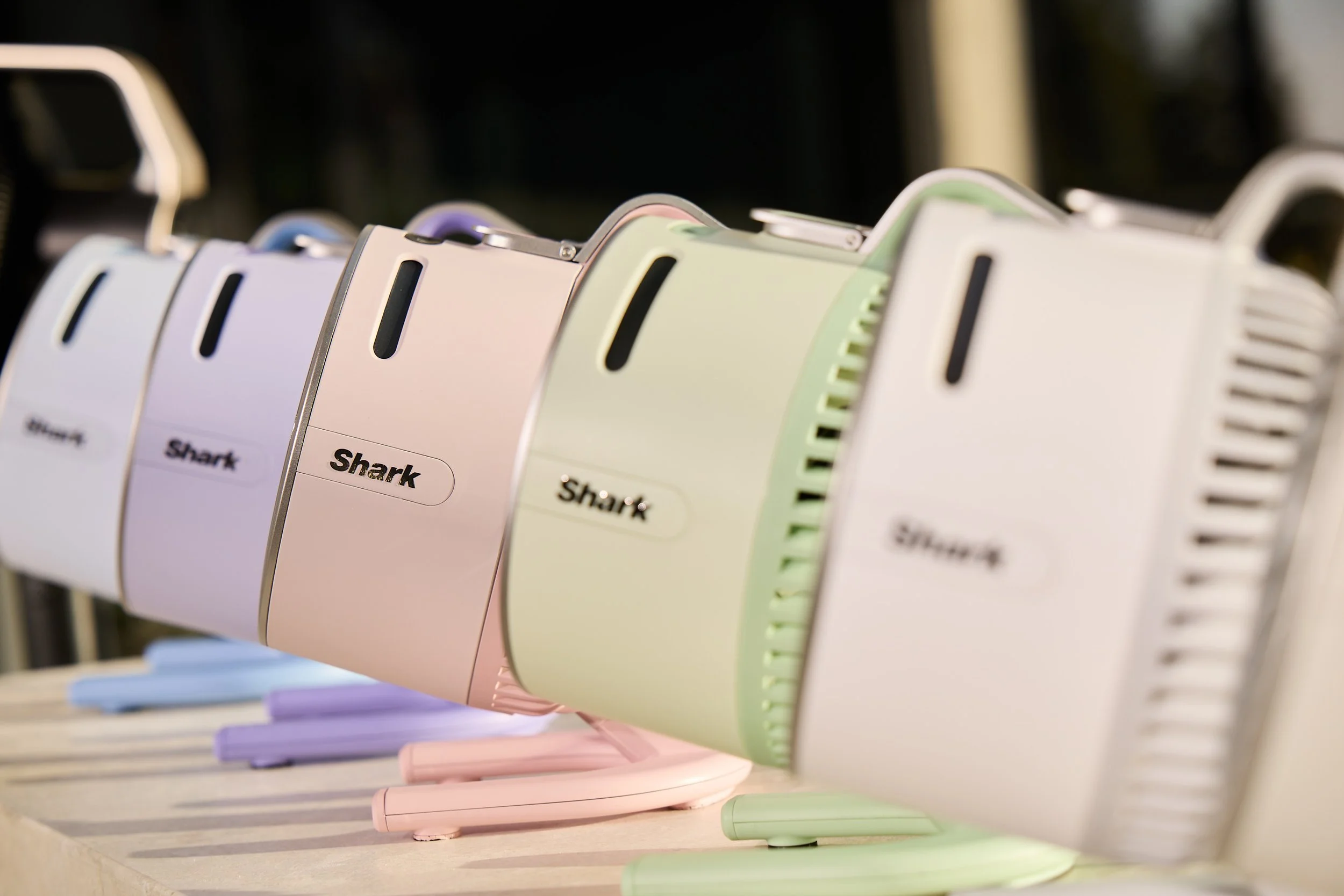 Row of pastel Shark brand hair dryers displayed on a table.