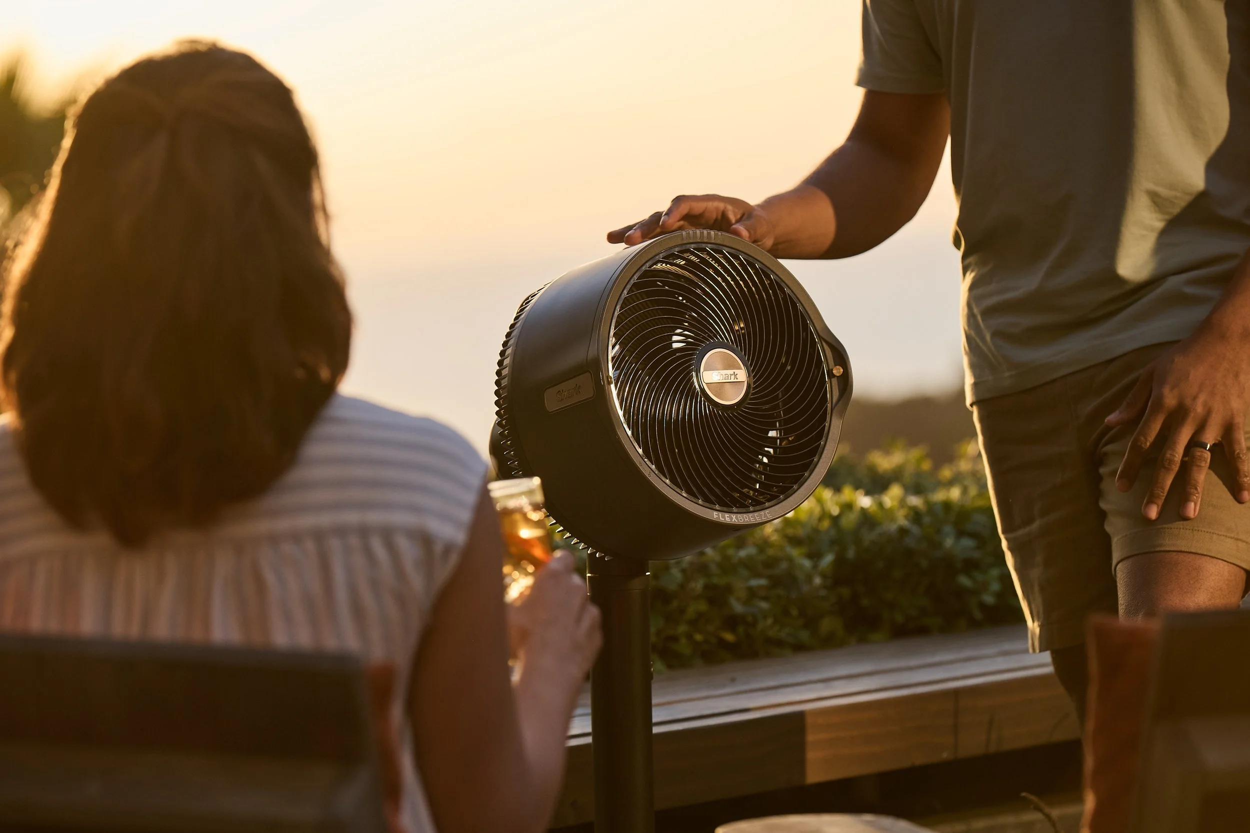 Two people with a fan in an outdoor setting at sunset.