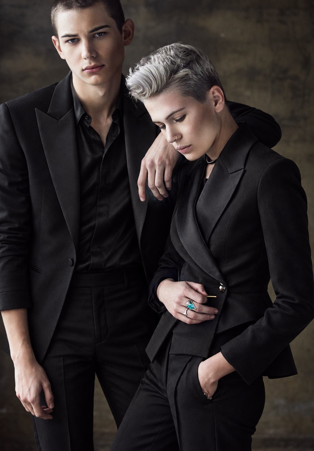 Two people wearing black suits against a textured backdrop