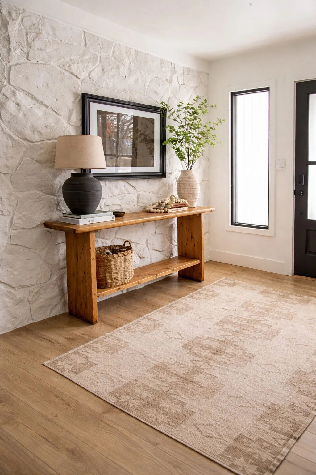 Modern ranch style entryway with white stone accent wall, rustic wood console table styling, neutral rug, and warm wood floors.