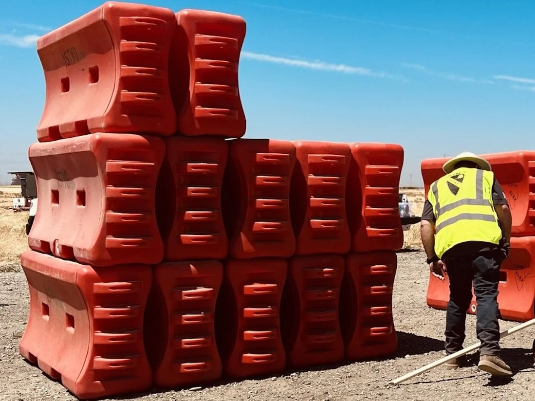 A 1st Vanguard worker wearing a yellow safety vest inspects temporary construction site barriers at the yard in Suisun City, CA