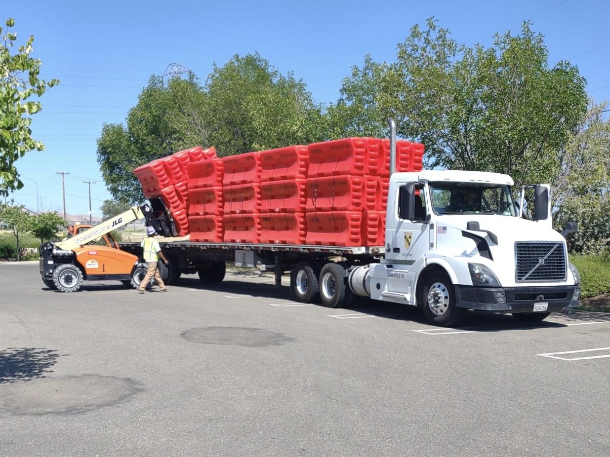 Water wall barrier being loaded onto flatbed semi truck for delivery
