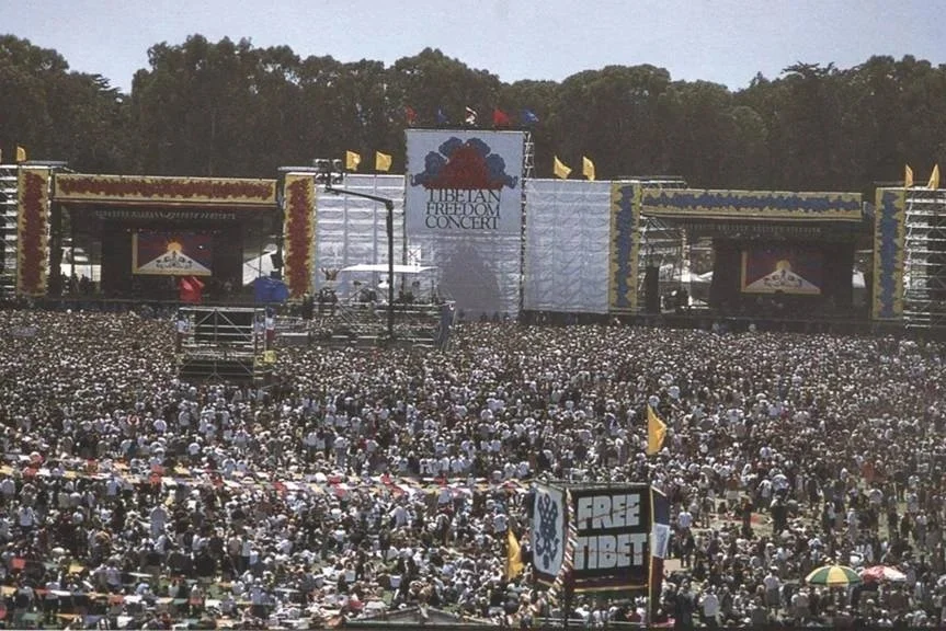 Large crowd gathered in front of a stage at a concert or event, with banners reading 'Tibetan Freedom Concert' and 'Free Tibet' visible.