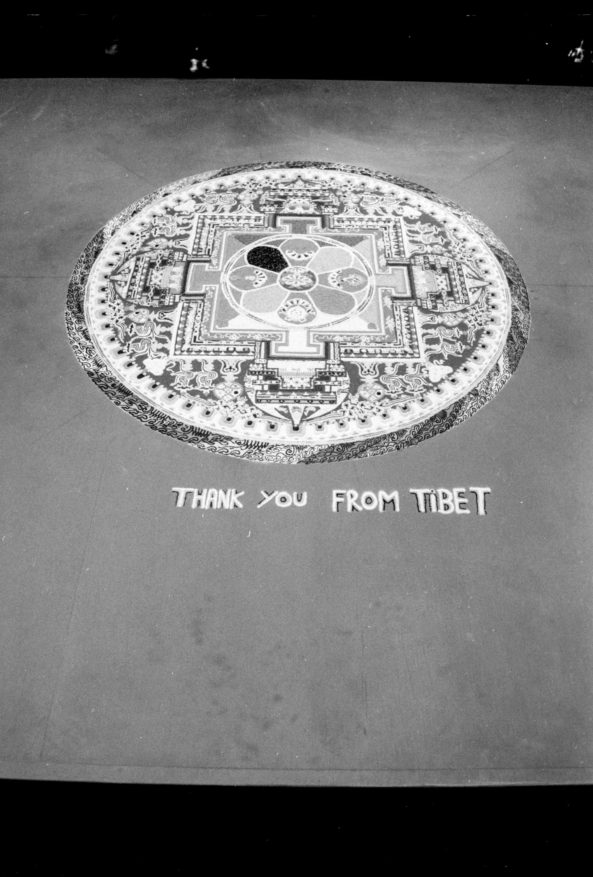 A traditional Tibetan colorful sand mandala on the floor with the words 'Thank you from Tibet' written below it.