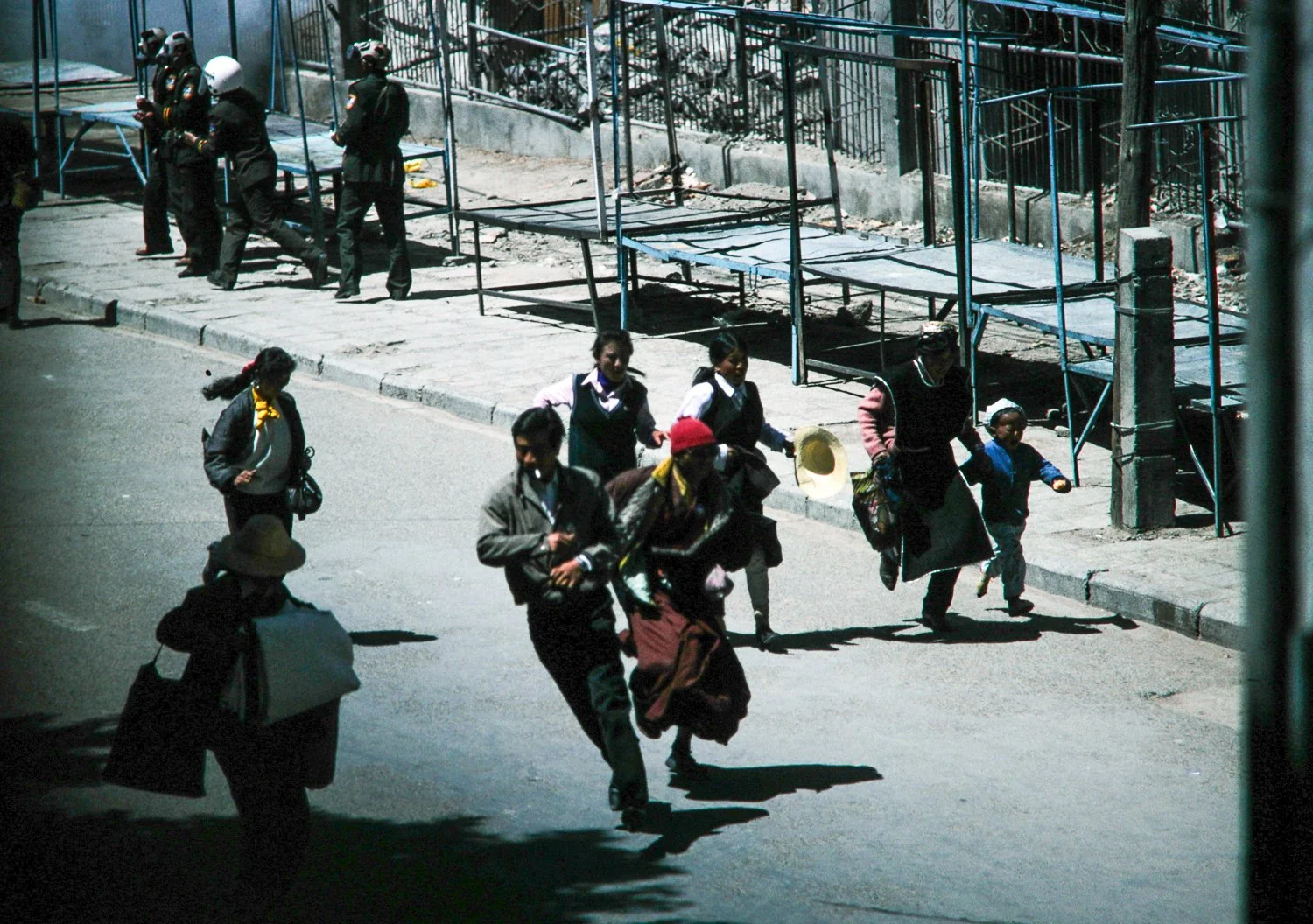 People walking on the street near a construction site with scaffolding. Two women and a child in the foreground, part of a group of pedestrians.