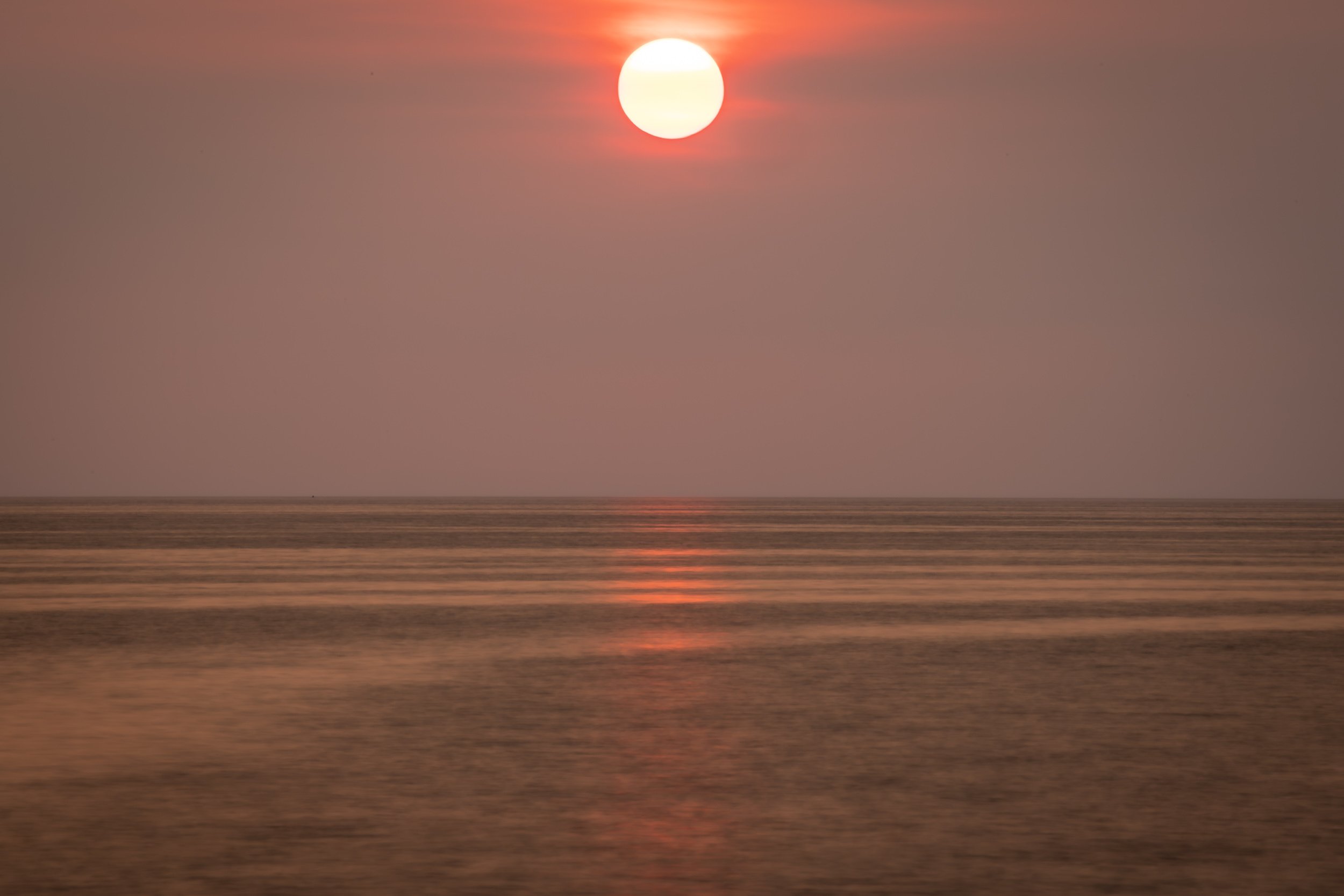 Fiery sun sets over calm, rippled waters painting the sky and lake in warm orange hues. Catawba Island, Ohio