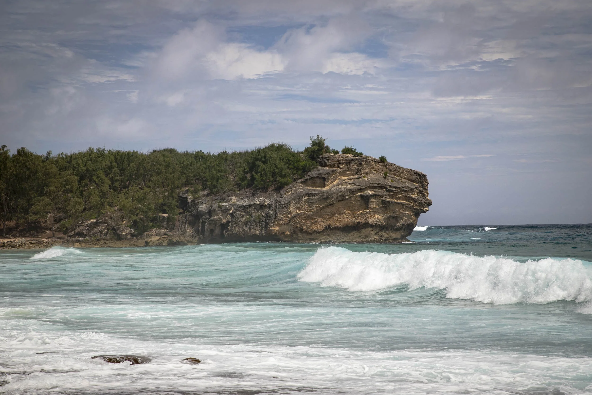 The image depicts a powerful wave crashing against a rocky cliff at Shipwreck Beach in Poʻipū, Kauaʻi, Hawaiʻi. 