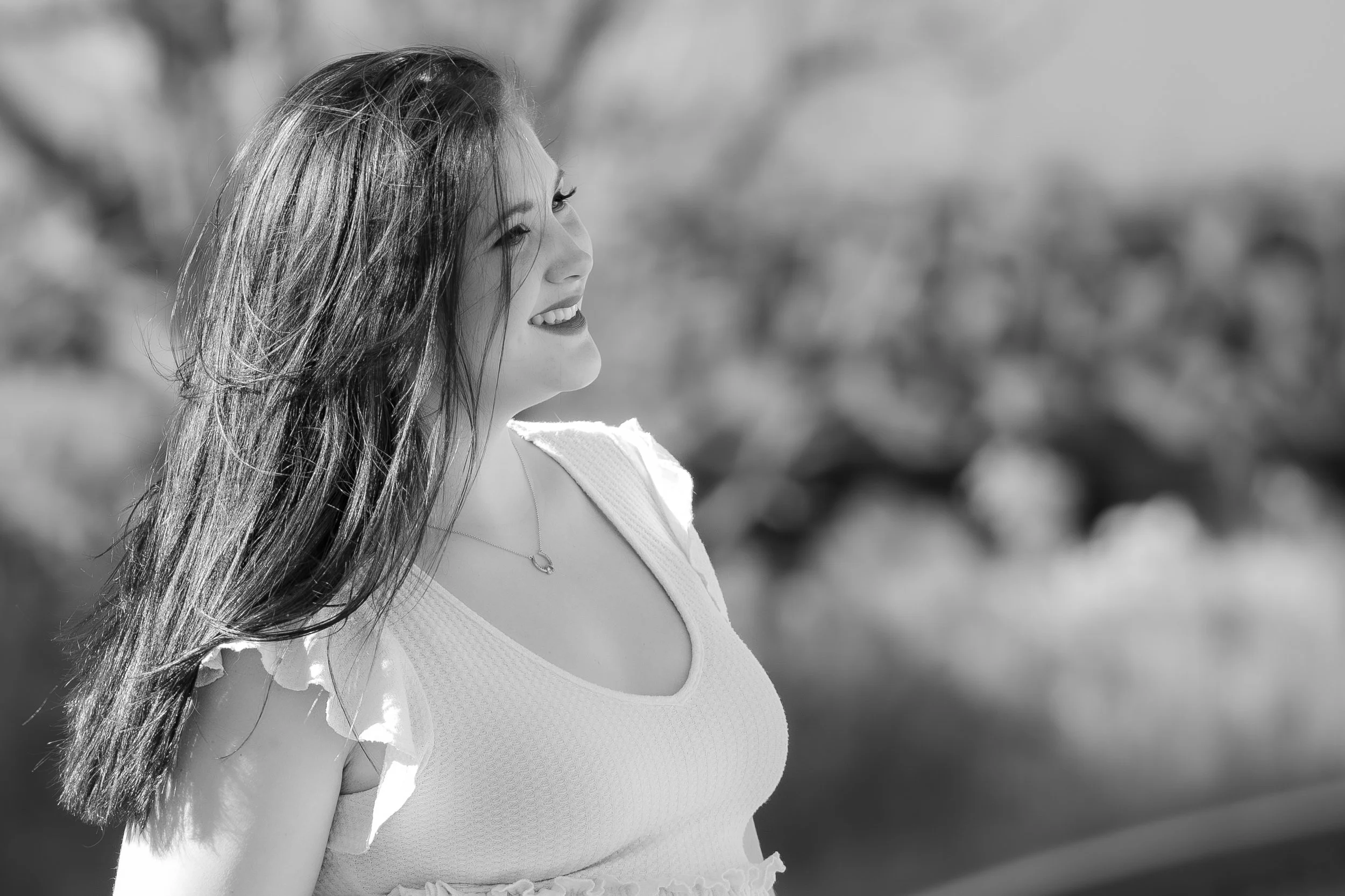 A young woman with long hair smiling outdoors in a black and white photo.