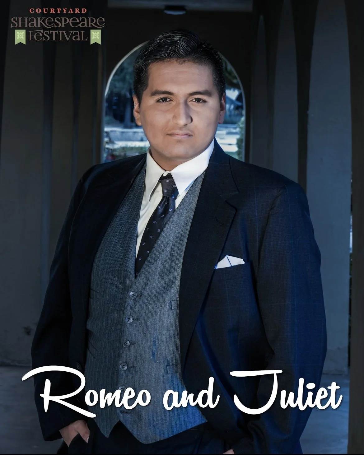 Mexican American man in a navy and gray suit portraying Mercutio in Shakespeare's Romeo and Juliet