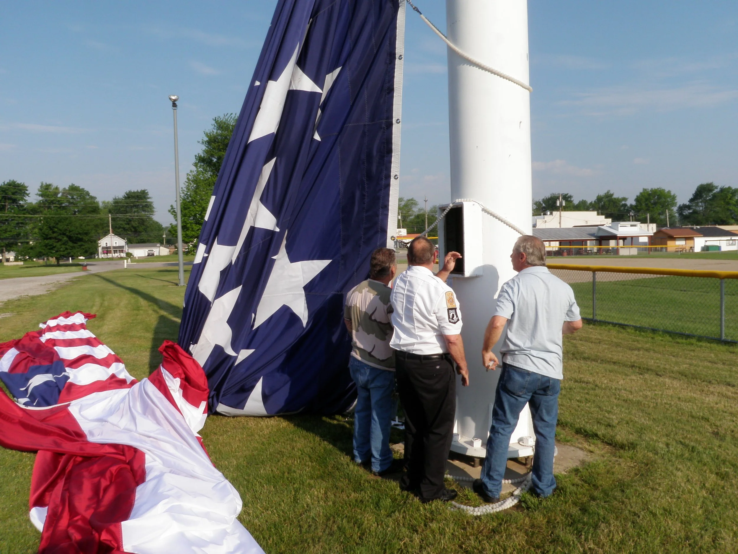 Group of men raising a large American flag on a flagpole in a grassy area.